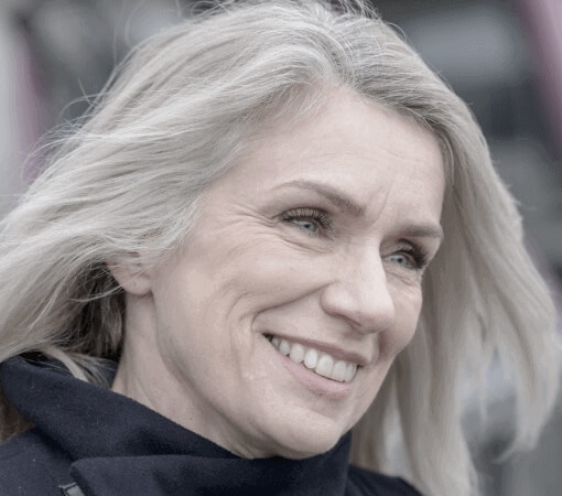 Close-up portrait of a smiling woman with silver hair outdoors.