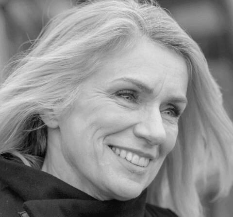 Close-up portrait of a smiling woman with silver hair outdoors.